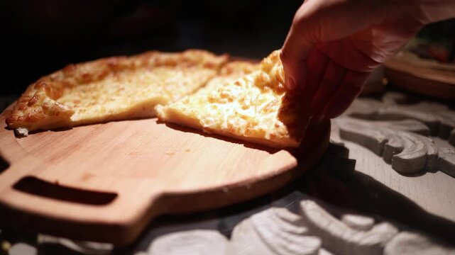 Hand taking piece of cheese khachapuri with hand while sitting at table close-up. Georgian food, Caucasian cuisine.