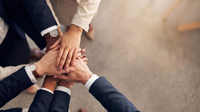 Business team places hands together in a stack to demonstrate unity and collaboration.