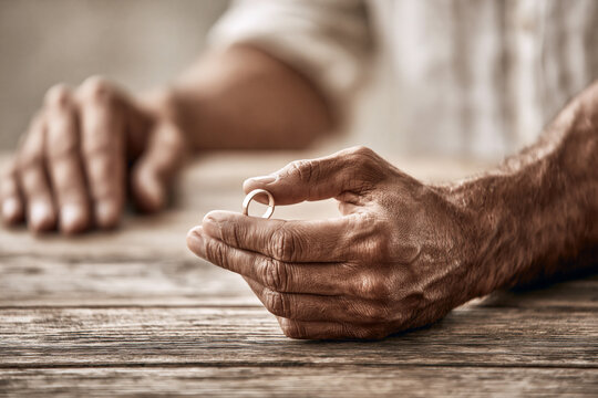 A pair of hands on a wooden table; one hand is removing a wedding ring, concept for couple problems.