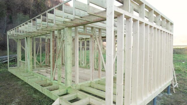 Drone aerial view of timber house frame in progress. Wooden beams, posts, and unfinished structure on grassy land capture residential construction site from above