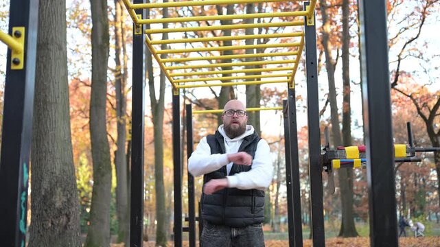 Man performs strength training on monkey bars surrounded by colorful autumn leaves, embracing fitness and fresh air in a serene park setting filled with tall trees.