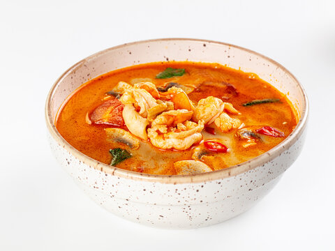 Spicy tom yum soup with prawns in speckled ceramic bowl on white background