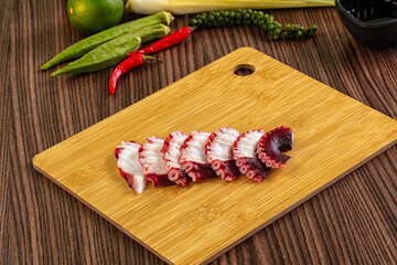 Sliced octopus tentacles on wooden cutting board with lime, chili, and herbs © Andrei Starostin