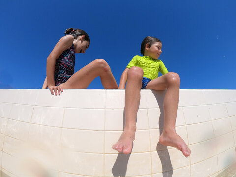 Two kids sitting on the edge of a swimming pool