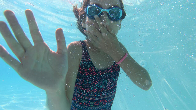 Young girl swimming underwater waving with her hands