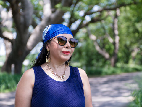 Elegant Mature Woman in Blue Dress and Sunglasses in a Green Park