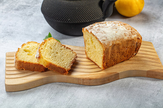 Sliced pound cake on wooden cutting board with lemon and black teapot background