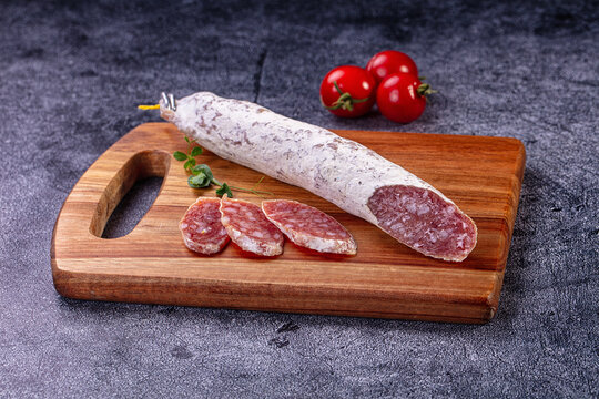 Fuet sausage on wooden cutting board with sliced pieces and cherry tomatoes