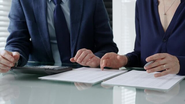 Business colleagues working together at a desk. Reviewing financial documents and utilizing a calculator for tax calculations or budget analysis