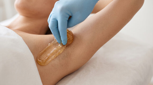 Extreme close-up of beautician applying natural sugar paste for armpit sugaring depilation, professional hair removal procedure in spa salon for smooth skin