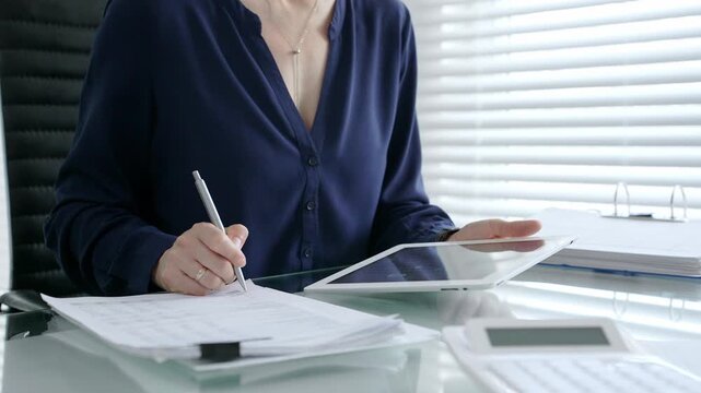 Businesswoman working on a tablet, analyzing financial data and electronic documents at a modern office desk, using digital technology for accounting and management tasks