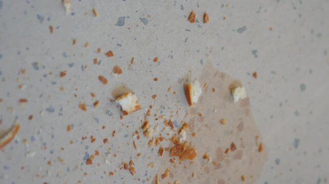 Close-up cinematic motion of small bread crumbs scattered on light-colored surface, ideal for culinary and abstract food themes