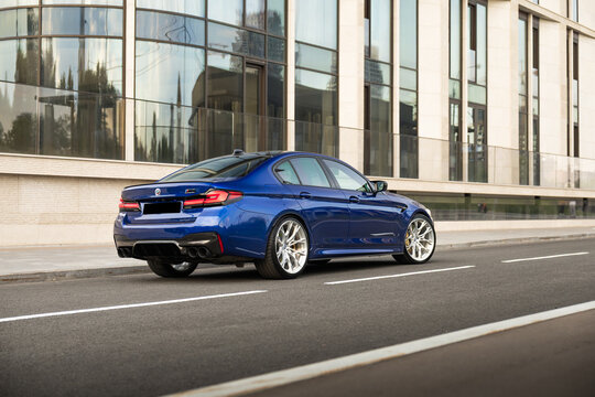 Blue BMW M5 performance sedan in a modern city, elegant exterior design, aggressive sporty styling, premium German automobile, sleek bodywork, urban atmosphere, high-quality automotive photography.