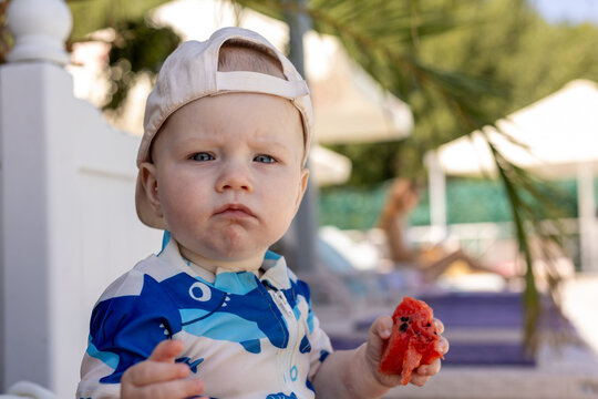 Baby boy in a shark swimsuit eating watermelon at the beach