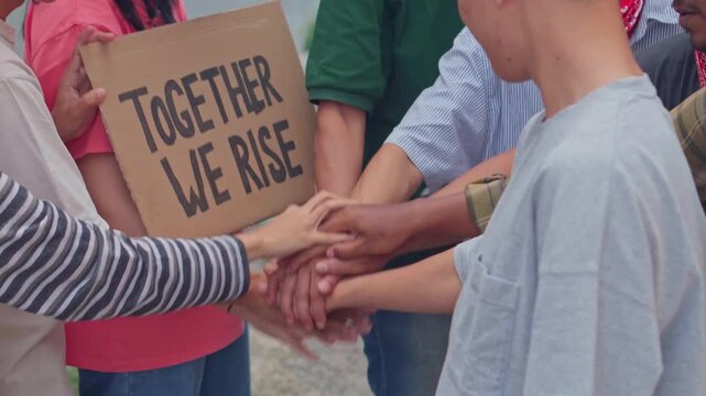Diverse group of young activists stacking hands in solidarity during protest demonstration for social change.