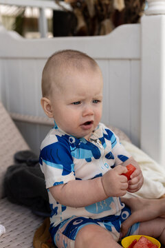 Curious baby in a blue whale swimsuit enjoys a refreshing piece of watermelon