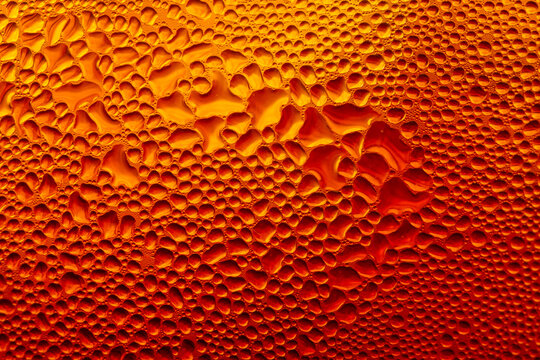 Macro water droplets condensation on cold amber glass background,A detailed macro photograph capturing water condensation droplets on a cold glass surface illuminated with warm amber and orange.