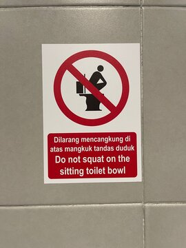 Bilingual prohibition sign warning against squatting on seated toilet bowl in public restroom.