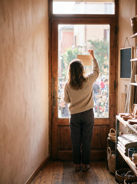 Woman hanging blank wooden sign on glass door of a rustic retail shop opening for local business