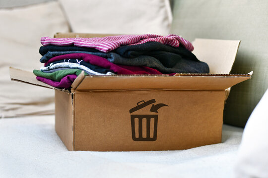 Box with folded clothes marked with trash bin icon as concept for textile waste and fast fashion disposal
