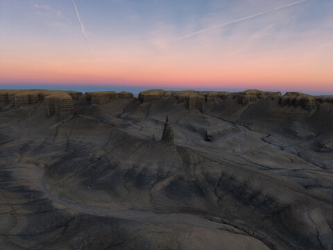 Aerial view of the rugged desert landscape with unique rock formations and eroded badlands under a soft sunset sky in Hanksville, Utah, United States.