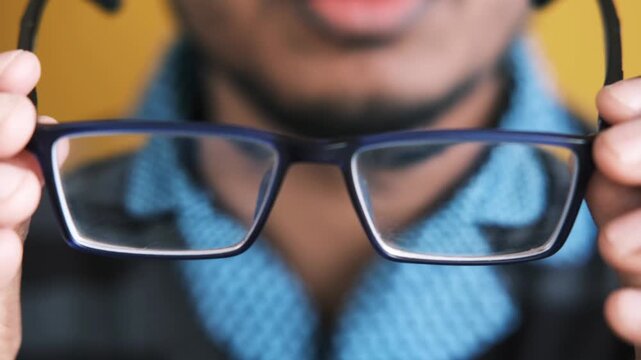 Man holding eyeglasses in front of face, close-up view with shallow depth of field