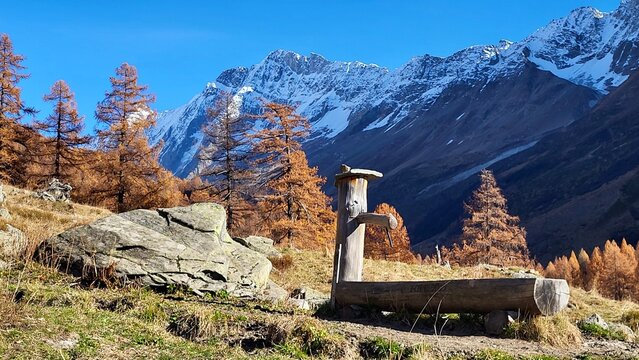 Picturesque autumn mountain landscape at Fafleralp in the L&ouml;tschental, Valais, Switzerland, featuring a traditional wooden fountain surrounded by golden-yellow larches and snow-capped mountains.