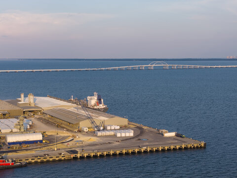 Aerial view of CEMEX Pensacola Cement Import Terminal with a cargo ship at the pier, industrial warehouses, and Pensacola Bay Bridge in Pensacola, Florida, United States.