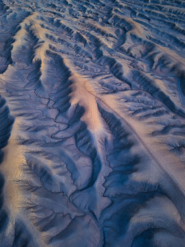Aerial view of Factory Butte showing the intricate, eroded badlands with deep gullies and ridges illuminated by soft golden hour light in Wayne County, Utah, United States.