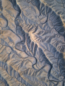 Aerial view of Factory Butte showcasing the intricate erosion patterns, deep ridges, and dramatic shadows of the badlands in Wayne County, Utah, United States.