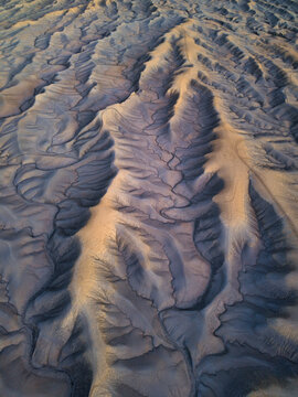 Aerial view of the rugged, eroded badlands surrounding Factory Butte, featuring intricate ridges, deep gullies, and dramatic shadows in Wayne County, Utah, United States.