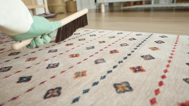 Close up of person wearing green rubber glove brushing beige patterned carpet at home, cleaning carpet with brush, housework, domestic cleaning chores, tidying home