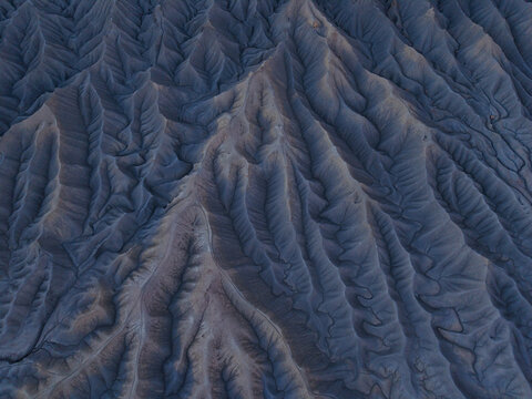 Aerial view of the rugged, eroded badlands of Factory Butte, showcasing intricate ridges, deep gullies, and dramatic shadows in Wayne County, Utah, United States.