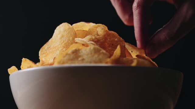 Slow motion closeup man hand taking potato chip from white bowl low angle shot