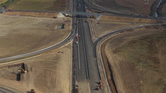 Aerial view of the Autostrada Moldovei A7 junction construction near Bacau, showing highway ramps, overpass, heavy machinery, and earthworks under soft daylight. 4K video.