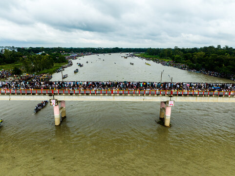 Aerial view of a crowded bridge spanning a wide river with lush green banks under a cloudy sky in Manikganj, Dhaka Division, Bangladesh.