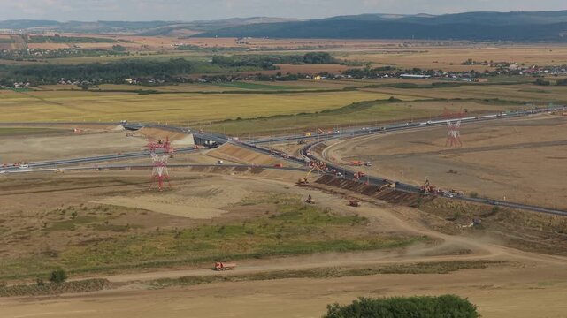 Aerial panoramic view of Autostrada Moldovei A7 Nod Bacau construction site with heavy machinery, highway interchange, and rural landscape in warm sunlight. 4K video.