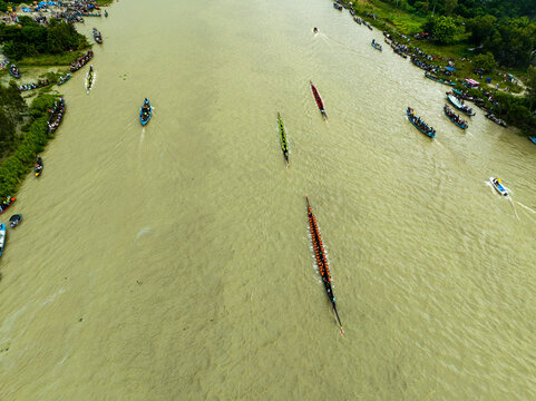 Aerial view of a traditional boat race on the river with long wooden boats filled with rowers and spectators lining the riverbanks in Manikganj, Dhaka Division, Bangladesh.