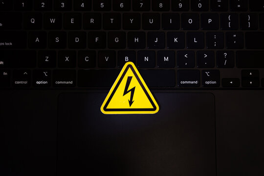 A high voltage warning triangle lies on a working laptop keyboard.