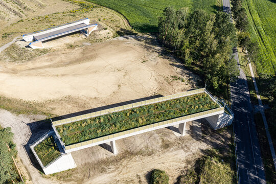 Aerial view of a green bridge wildlife crossing under construction spanning over a road with surrounding fields and trees in Celle, Germany.