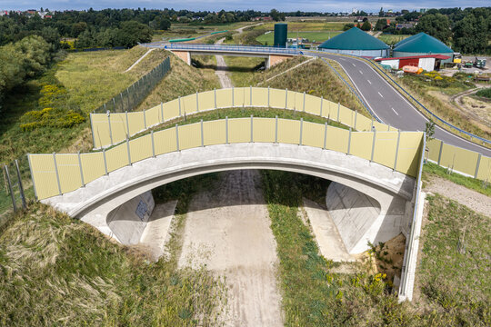 Aerial view of a wildlife crossing bridge over a path with a bypass road and biogas plant in the background in Celle, Germany.