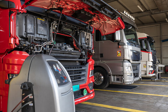 Truck service.  Professional truck service garage with a red heavy vehicle undergoing engine inspection and air conditioning maintenance inside a clean industrial workshop.