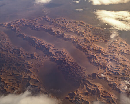 Aerial view of the vast Sahara Desert featuring rolling sand dunes, arid terrain, and scattered clouds under soft light in Algeria.