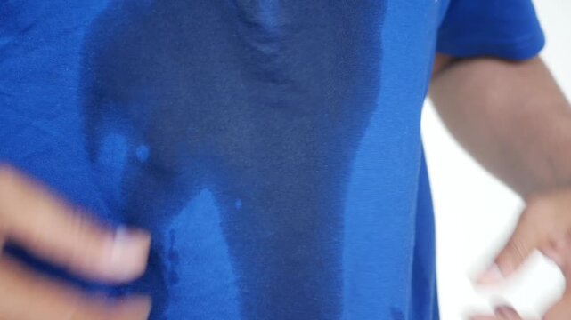 Man pulls sweaty blue t-shirt on sides showing sweat stains from workout or heat
