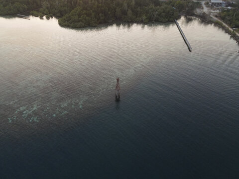 Aerial view of Waisai Harbour navigational beacon surrounded by clear turquoise water and lush mangrove coastline in Raja Ampat, Papua Barat Daya, Indonesia.