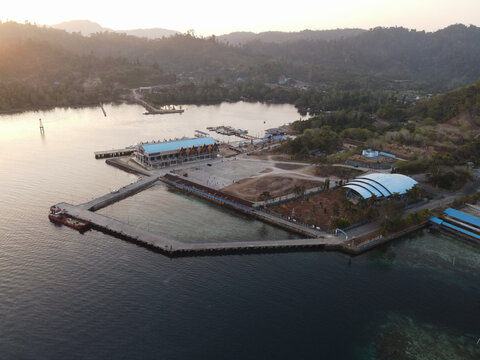 Aerial view of Waisai Harbour with its modern terminal building, concrete pier, and surrounding coastal landscape during golden hour in Raja Ampat, Papua Barat Daya, Indonesia.