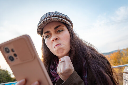 Female holding mobile phone and reacting aggressively to unexpected online content. Human emotions and communication concept.
