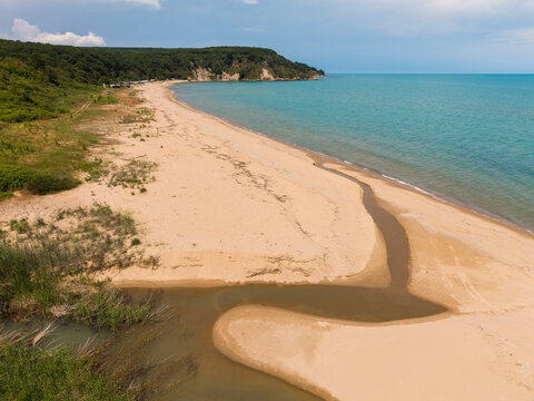 Aerial view of Kara Dere beach with a stream flowing into the Black Sea, surrounded by lush green hills and sandy coastline in Byala, Varna, Bulgaria.