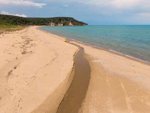 Aerial view of Kara Dere beach with a small stream flowing into the Black Sea, sandy shoreline, and green hills in the background in Byala, Varna, Bulgaria.