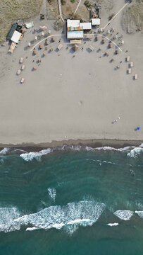 Aerial view of Ada Bojana beach with rows of umbrellas, wooden beach bars, and gentle waves washing onto the sandy shore in Ulcinj Municipality, Montenegro.